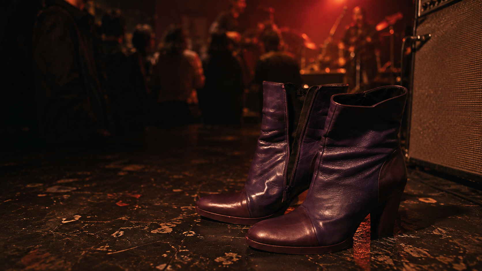 Purple leather boots on the floor of CBGBs, with a dimly lit concert crowd and stage equipment behind them.