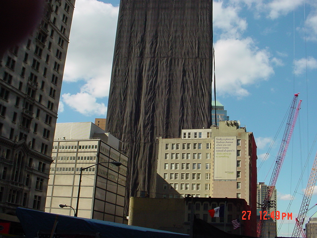 Lower Manhattan after September 11, with the damaged Bankers Trust building wrapped in black netting and construction cranes nearby.