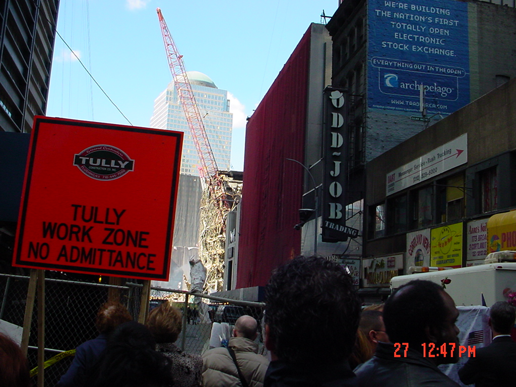 A crowd near Century 21 faces a fenced work zone, construction cranes, and damaged buildings in Lower Manhattan after September 11.