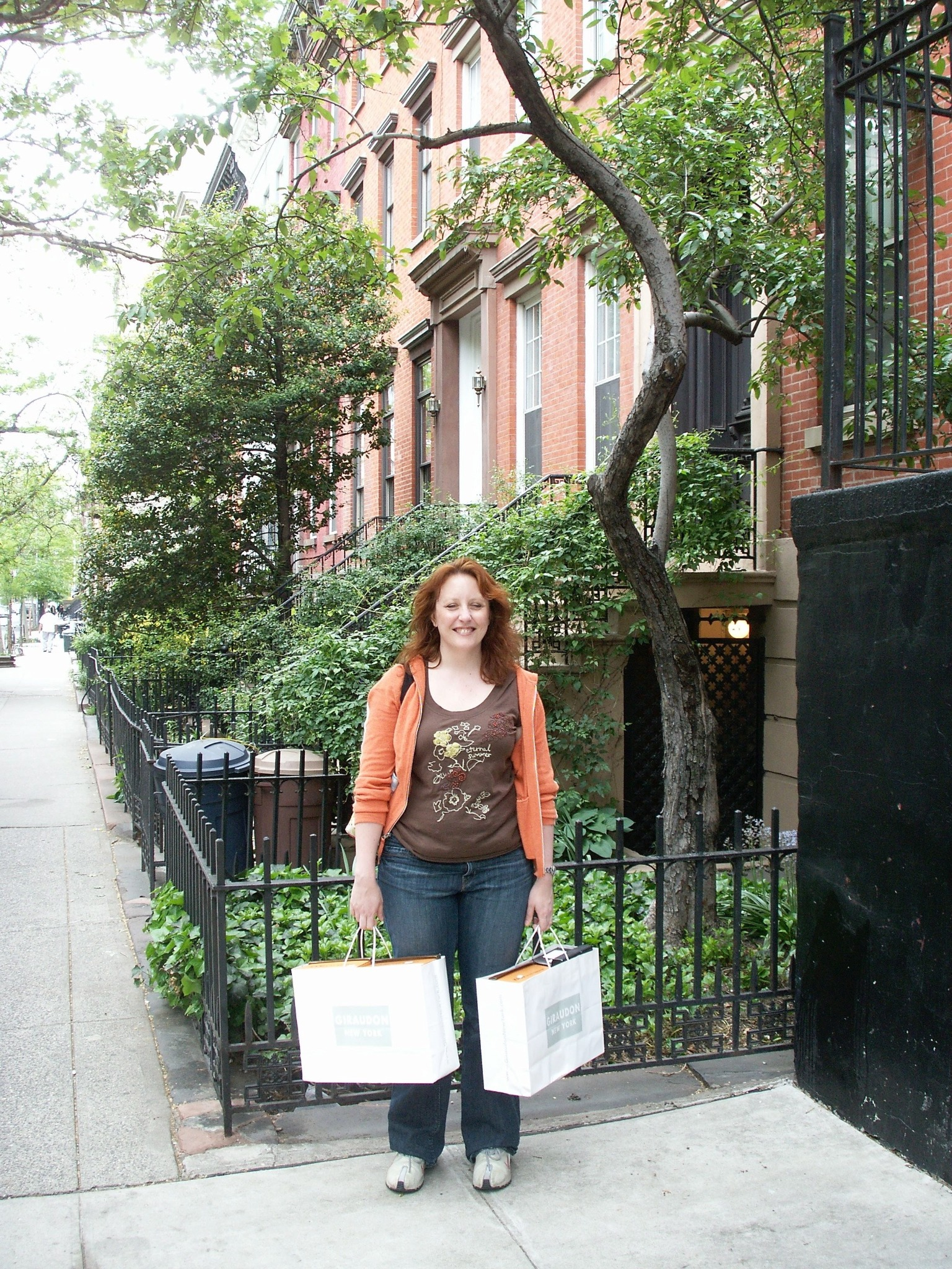 Jenn Day standing on a tree-lined Manhattan sidewalk with shopping bags.