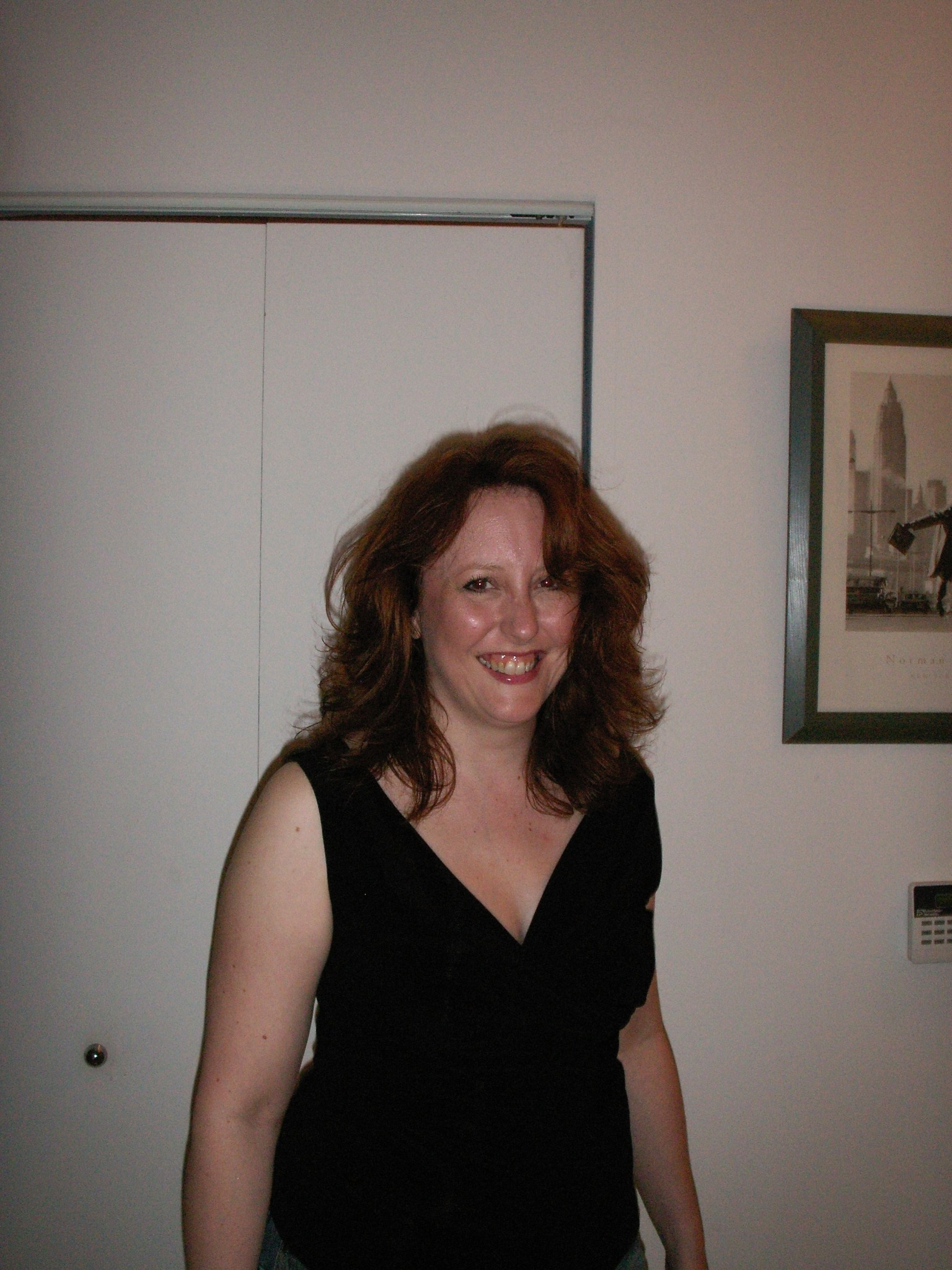 Jenn Day smiling in a black dress in her New York apartment, with a framed Manhattan skyline print behind her.